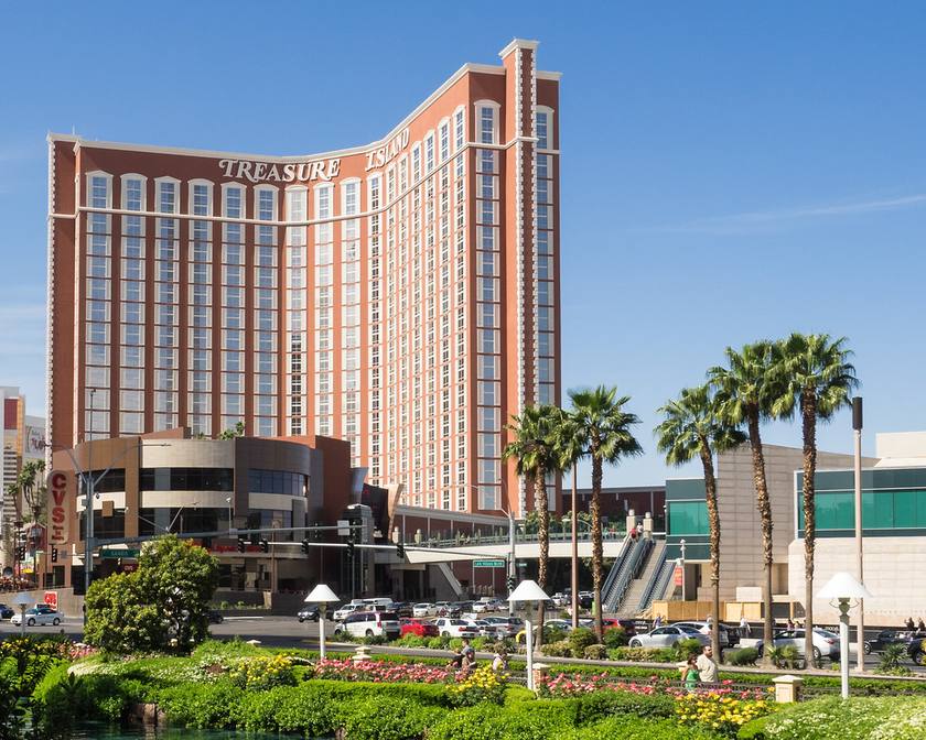 The Treasure Island hotel tower with its Treasure Island sign, palm trees and a blue sky