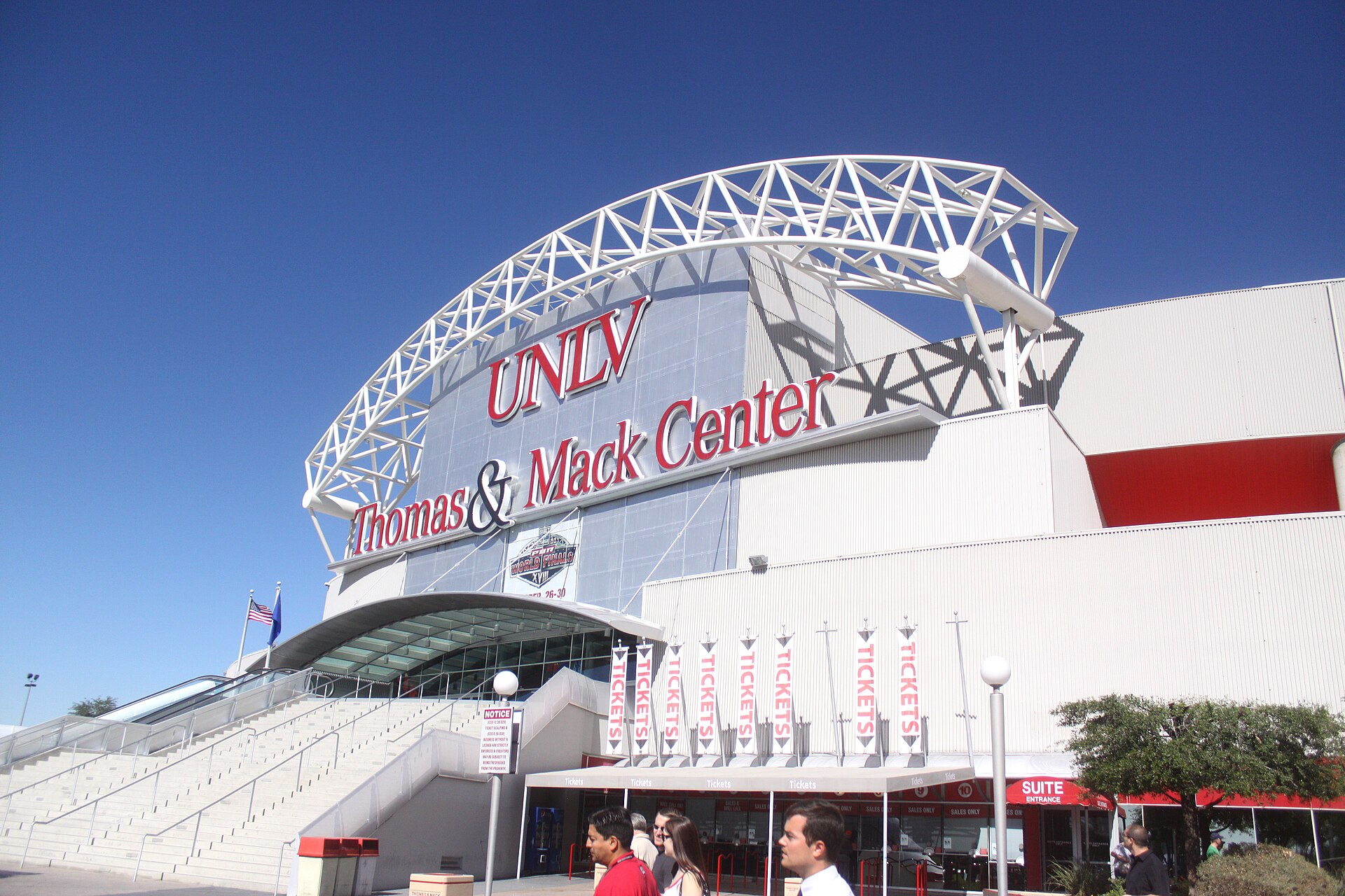 The Thomas and Mack Center entrance on the UNLV campus with its white steel arch and red UNLV lettering under a blue sky