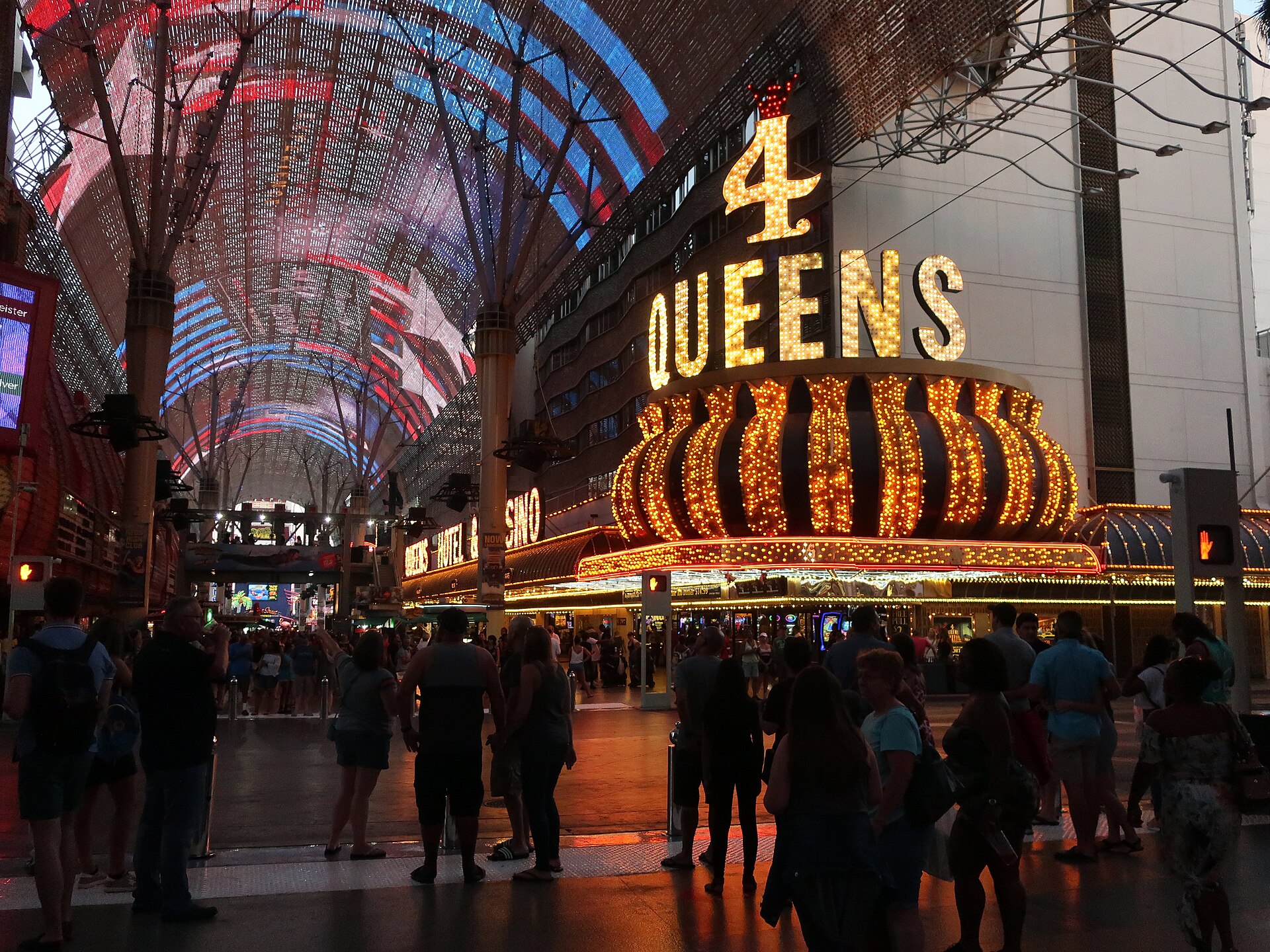 Crowds walk under the lit Fremont Street Experience canopy beside the glowing Four Queens casino sign at night