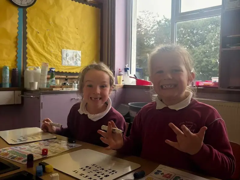 Two smiling pupils with mini whiteboards and cubes during an addition activity