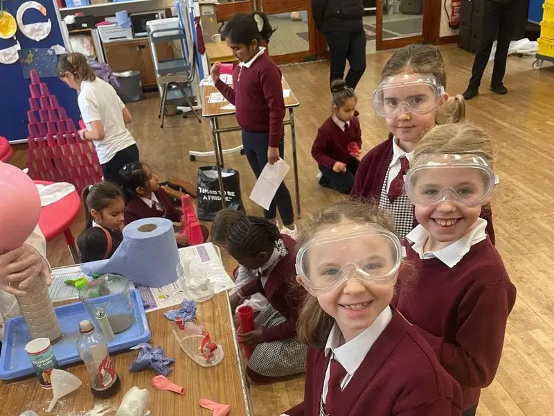 Pupils in safety goggles beside a table of science experiments