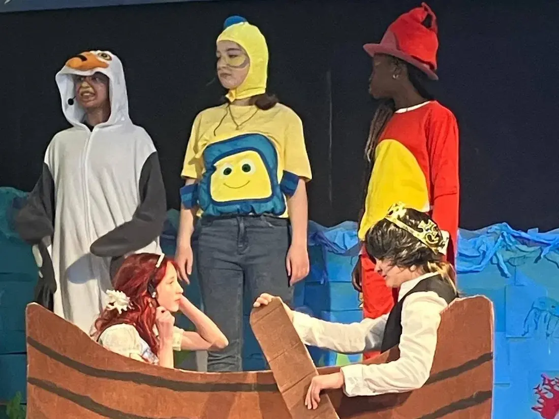 Pupils in costume on stage in a cardboard boat during The Little Mermaid