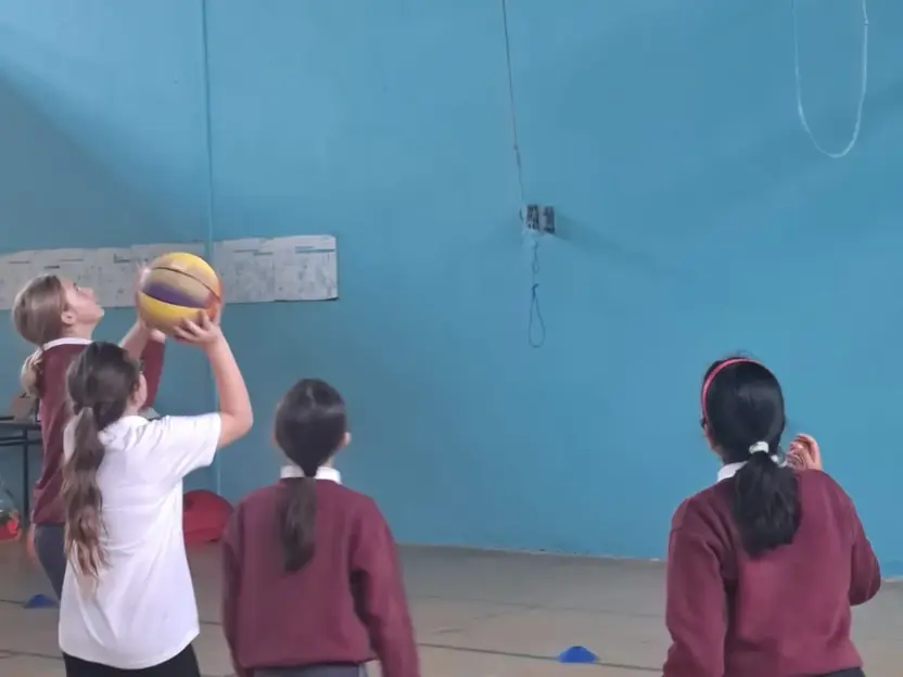 Pupils practising basketball shots in a sports hall