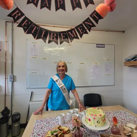 Elma beside a table of cakes under a Happy Retirement banner