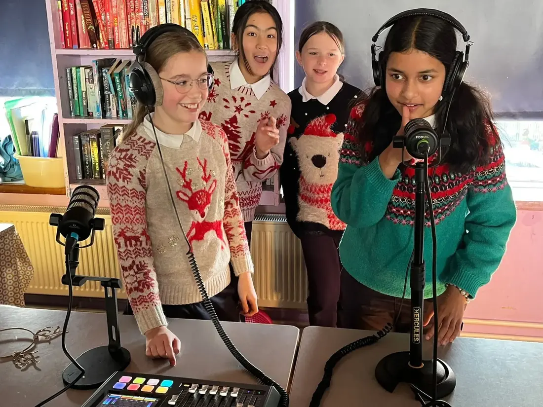 Pupils with headphones and microphones recording the 6th Class podcast