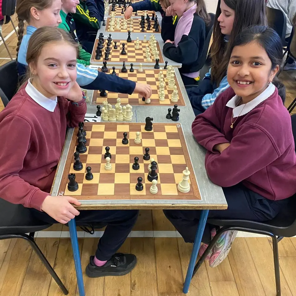 Two pupils smiling across a chess board at a schools tournament