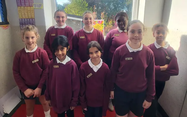 The 2026/27 Student Council: eight pupils in school uniform standing in front of a classroom window