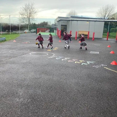 1st and 2nd Class pupils doing movement activities at stations in the school yard