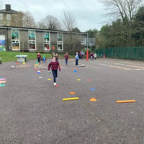 1st and 2nd Class pupils doing movement activities at stations in the school yard