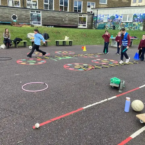 1st and 2nd Class pupils doing movement activities at stations in the school yard