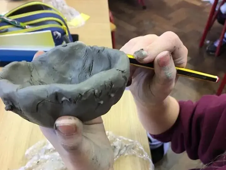 A pupil shaping a clay pot with a pencil