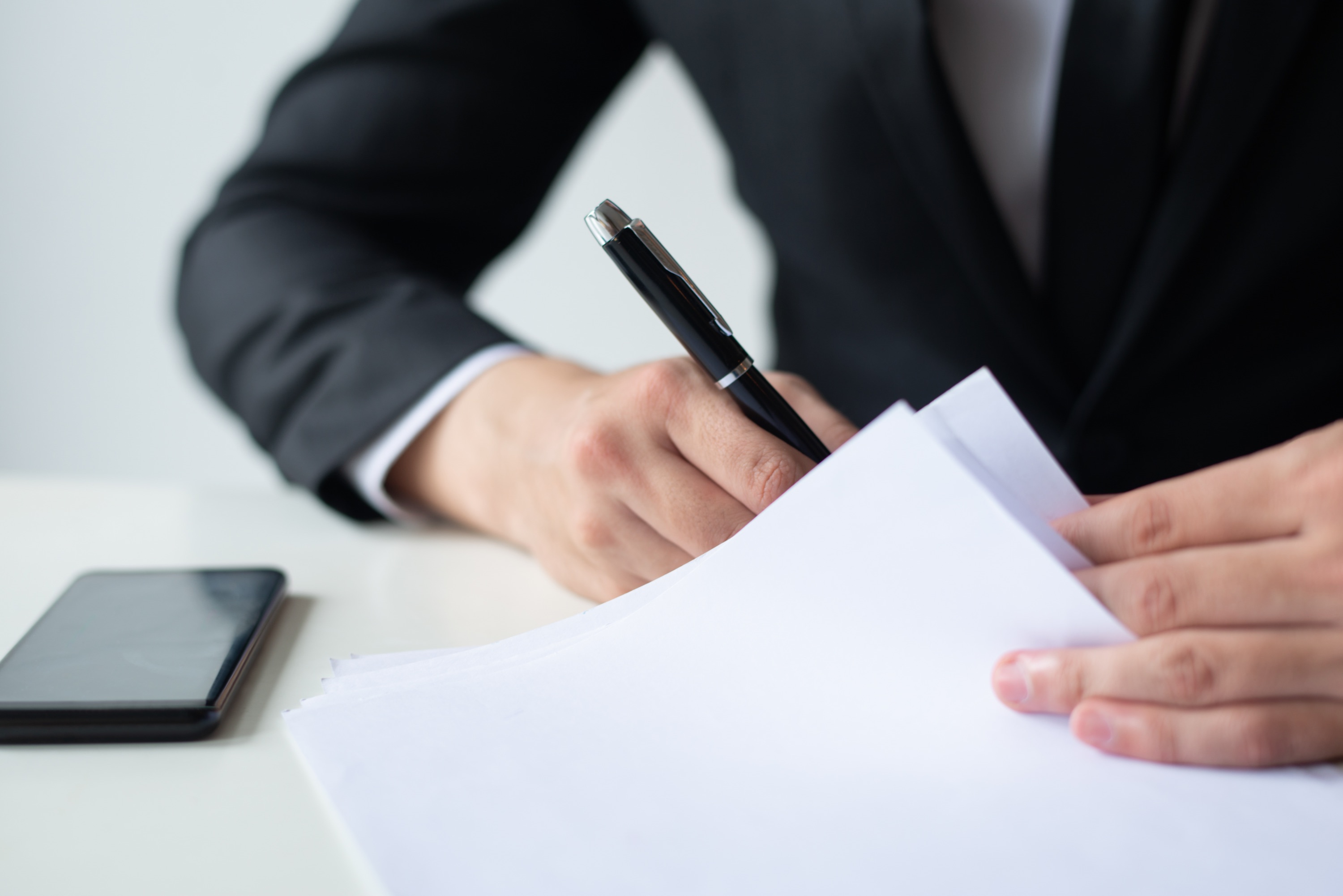 Professionista in giacca e cravatta che firma un documento alla scrivania