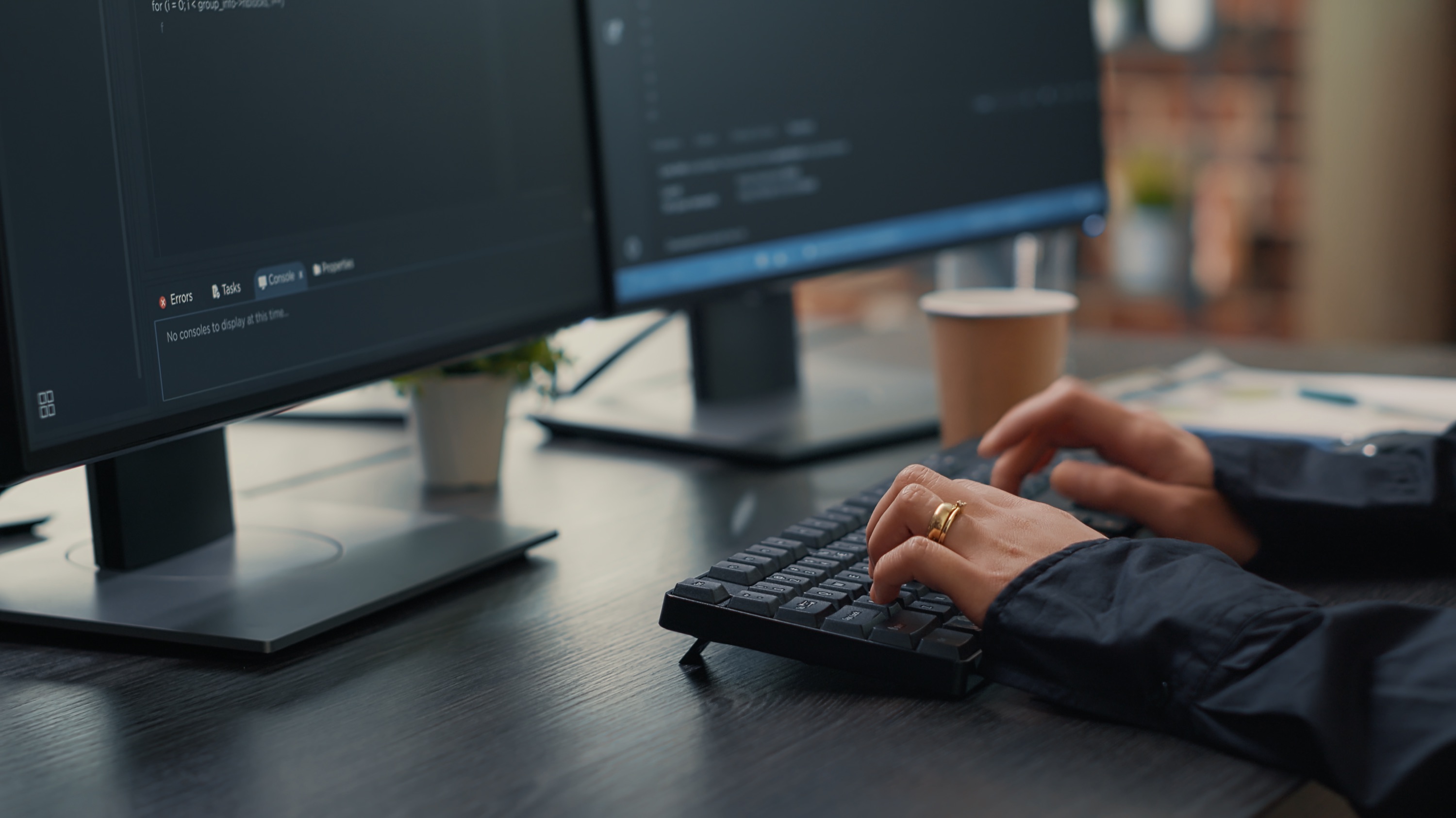 Mani che scrivono codice su una tastiera davanti a due monitor in un ufficio