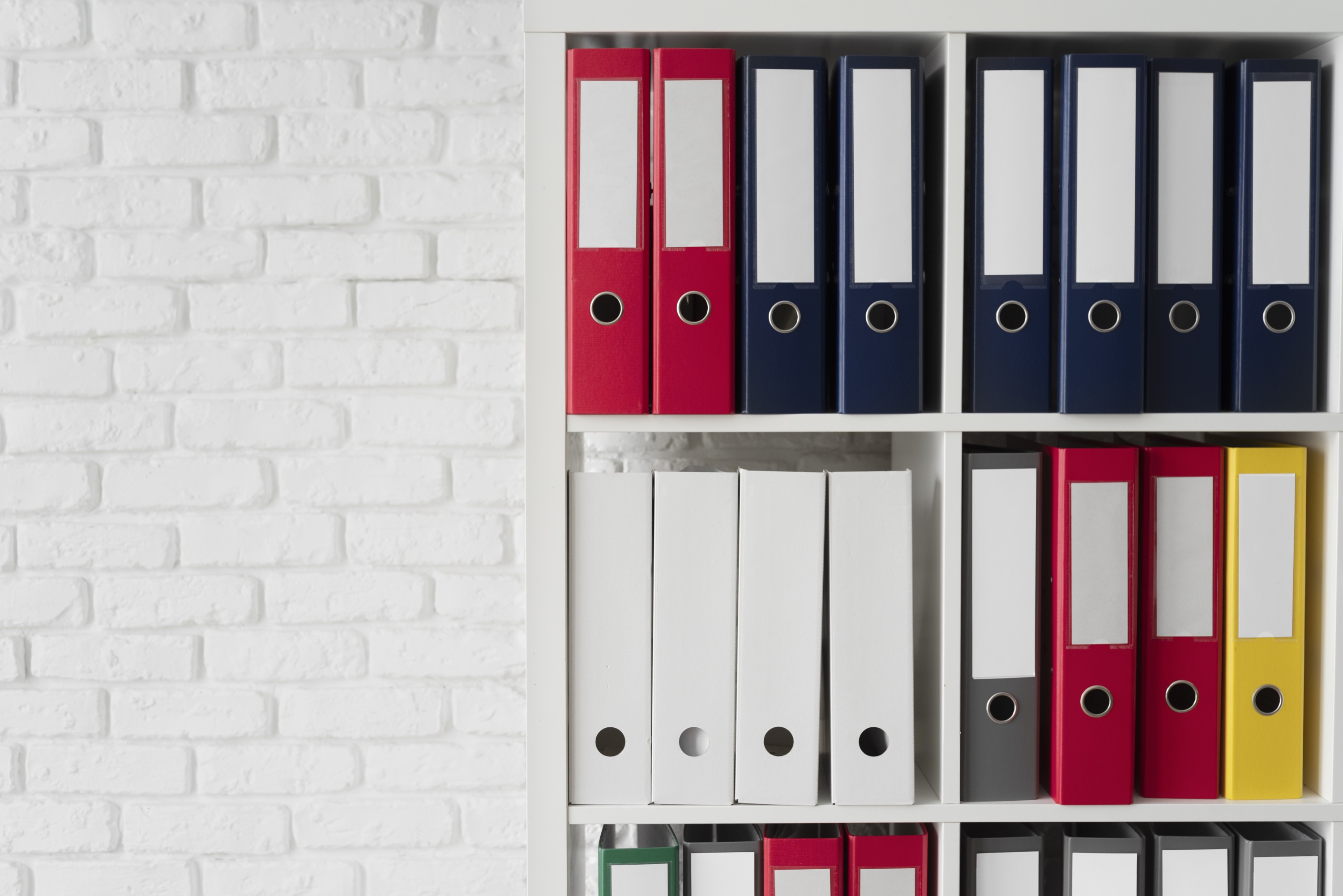 Raccoglitori colorati per documenti allineati su una libreria bianca