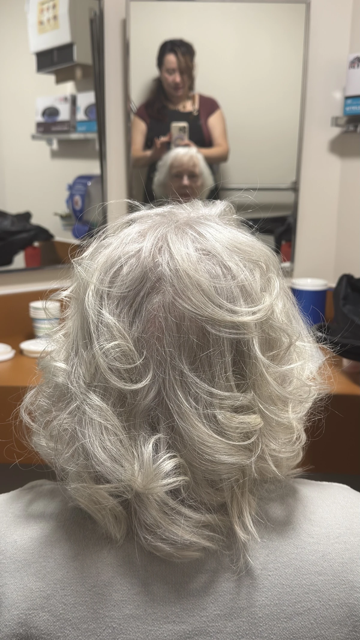 The back of a softly styled silver haircut, with Aura visible in the mirror