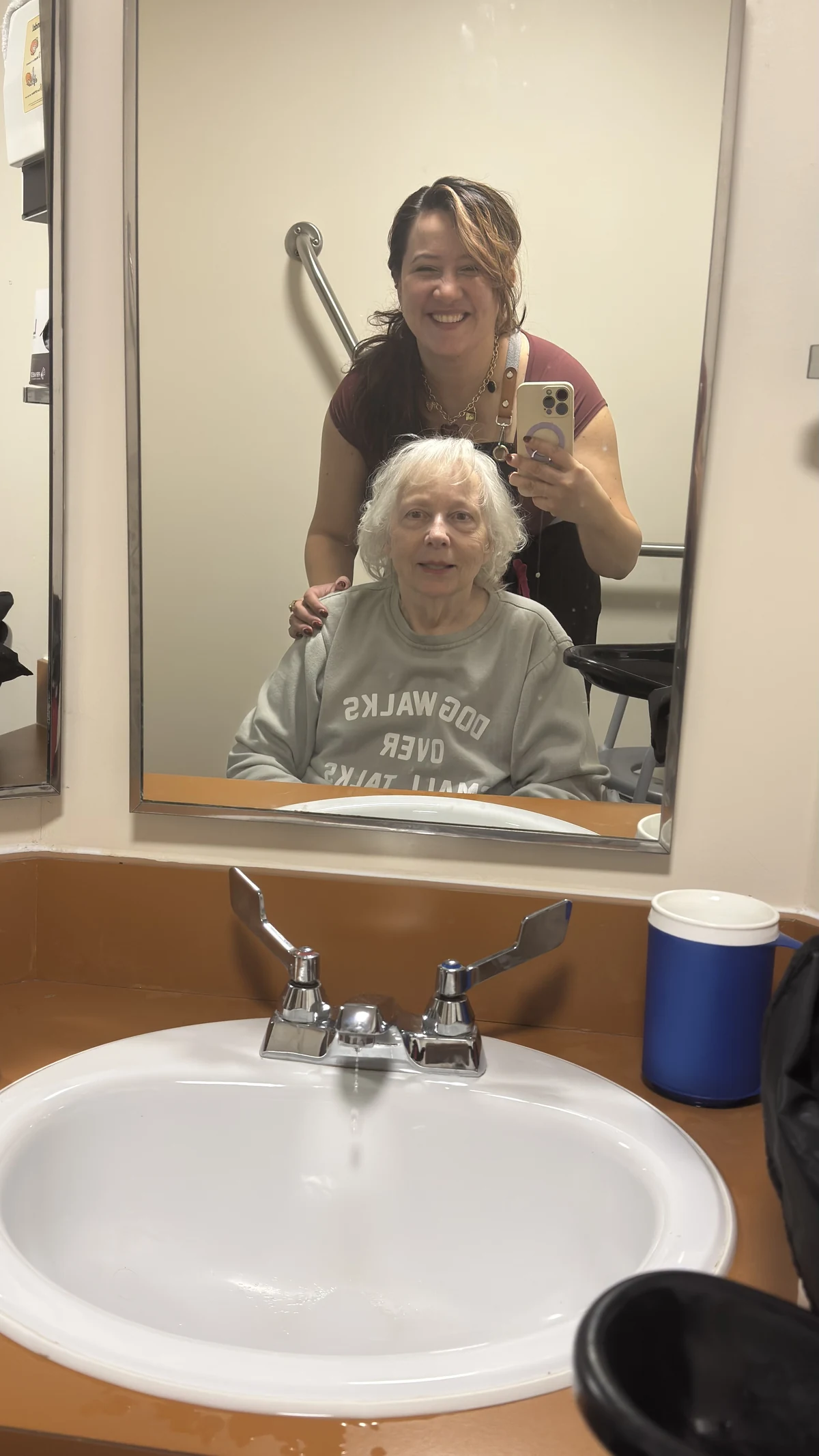 Aura photographing a finished hairstyle in a mirror, with her client seated in front