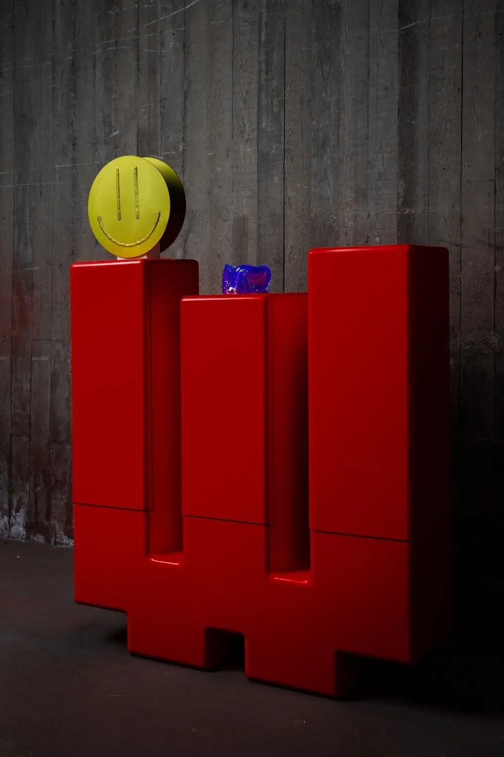 Red Inferno cabinet with a yellow smiley vase and a blue glass object on top