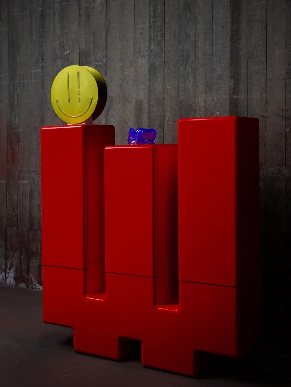 Red Inferno cabinet with a yellow smiley vase and a blue glass object on top