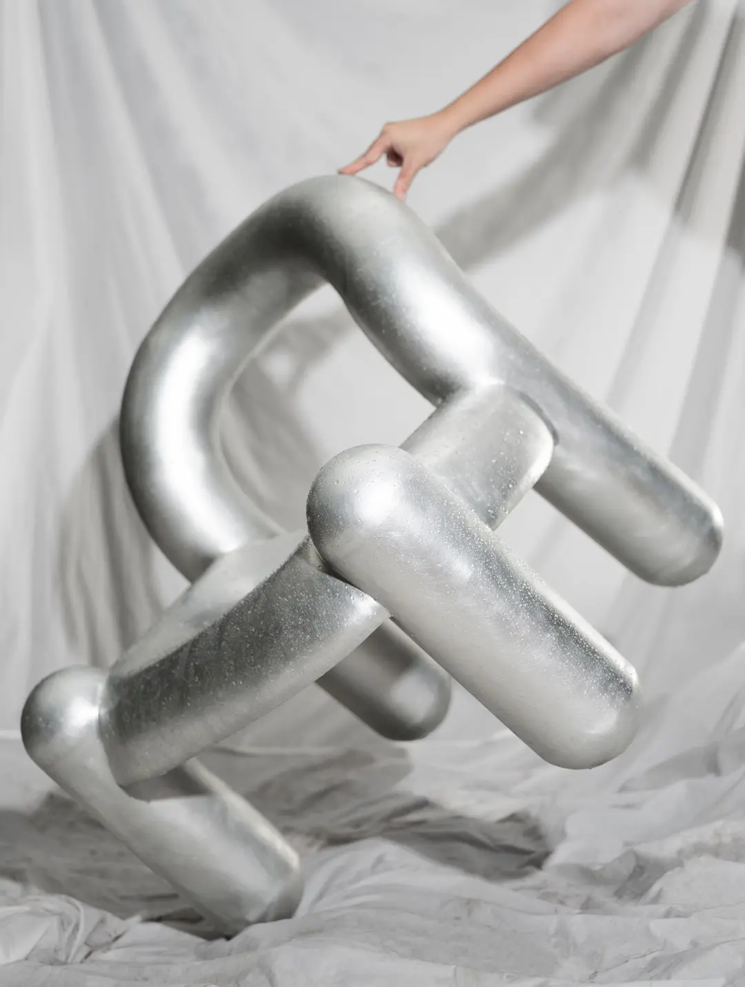 A hand holding the silver Reality chair against a white drape