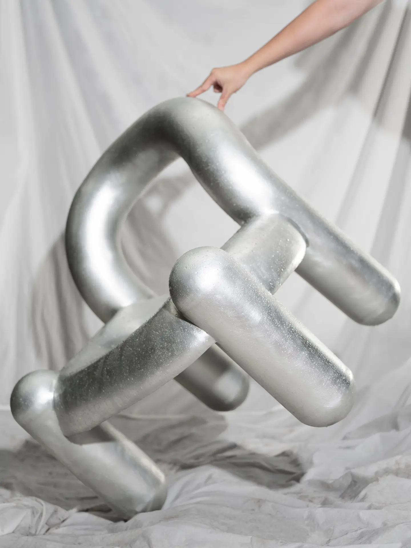 A hand holding the silver Reality chair against a white drape