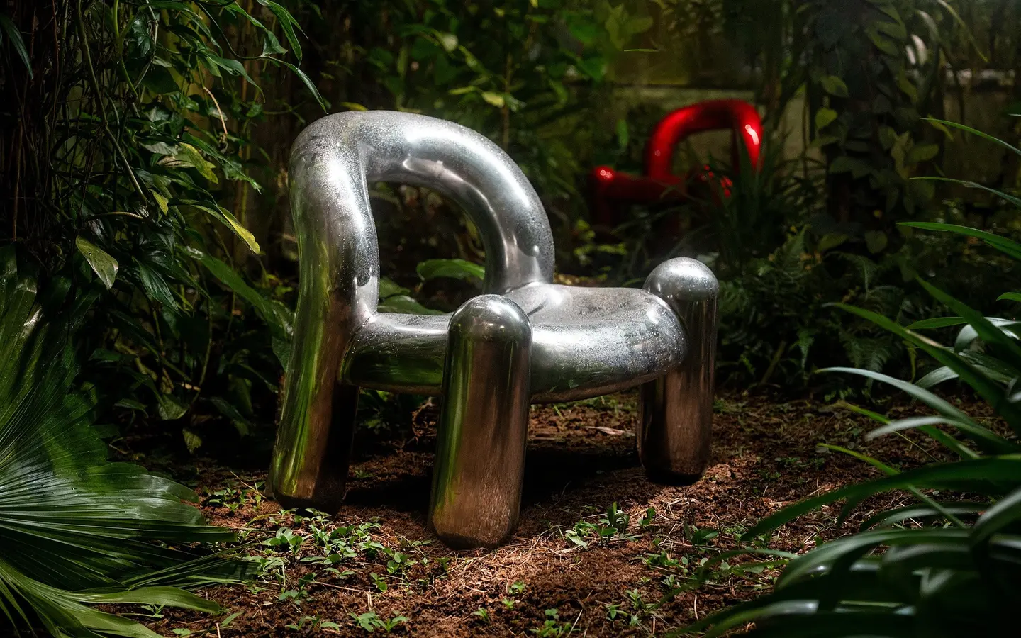 Silver Reality chair in the greenery with a red one behind it