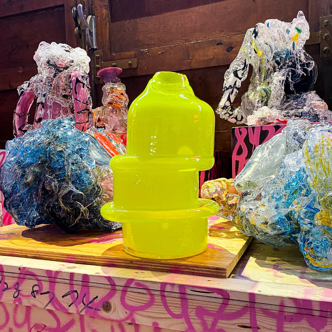 Yellow Skew sculpture among glass objects on a painted table