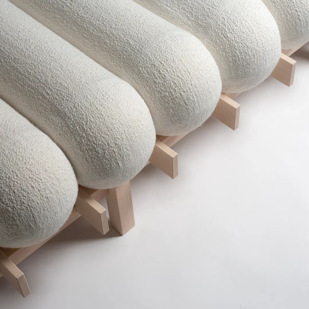 Row of white bouclé cushions resting on the slatted beech frame