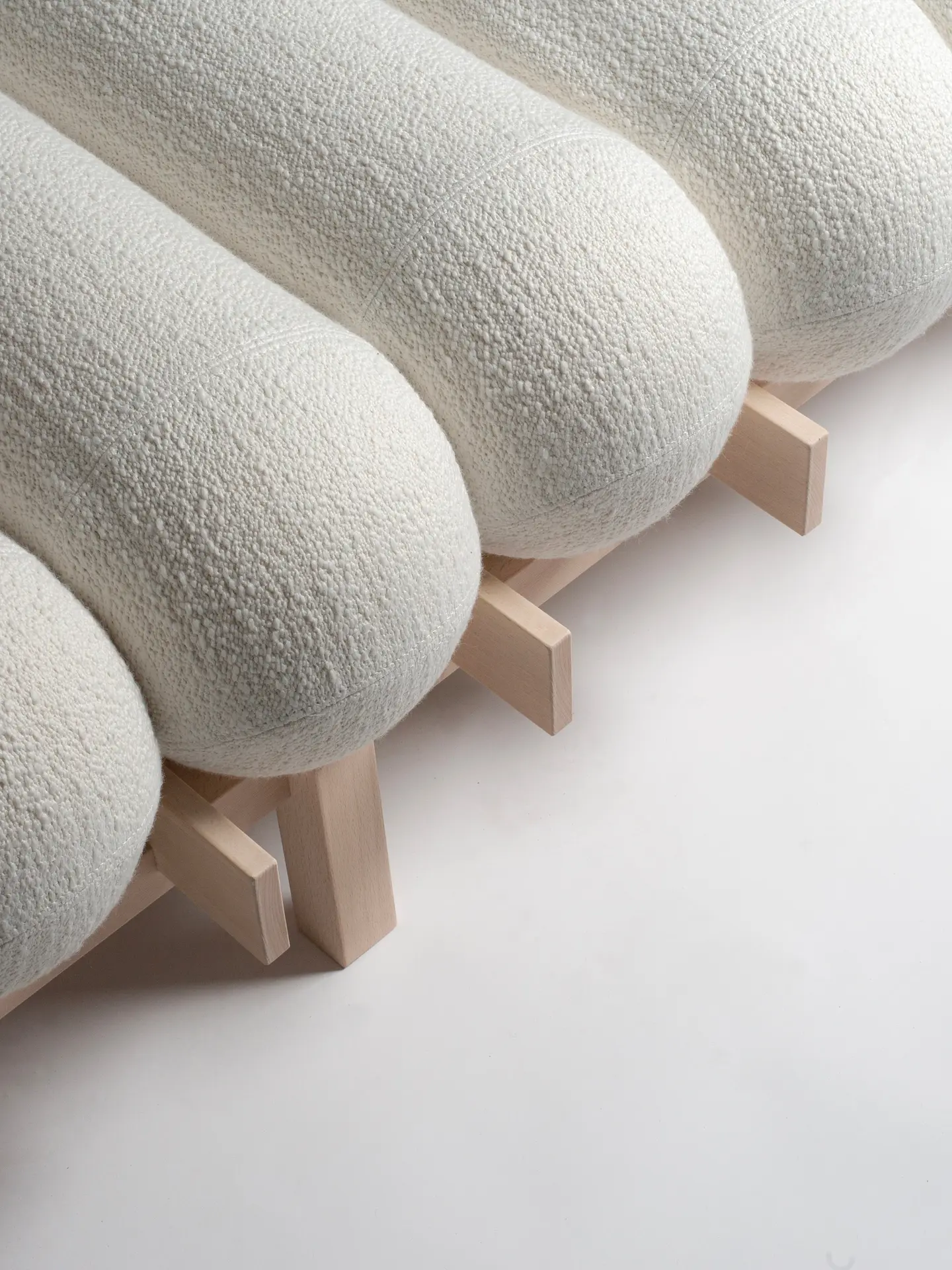 Row of white bouclé cushions resting on the slatted beech frame