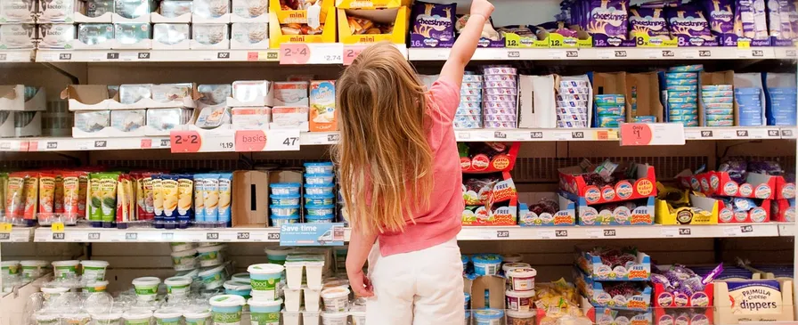 A young girl reaching up to a supermarket shelf of packaged foods