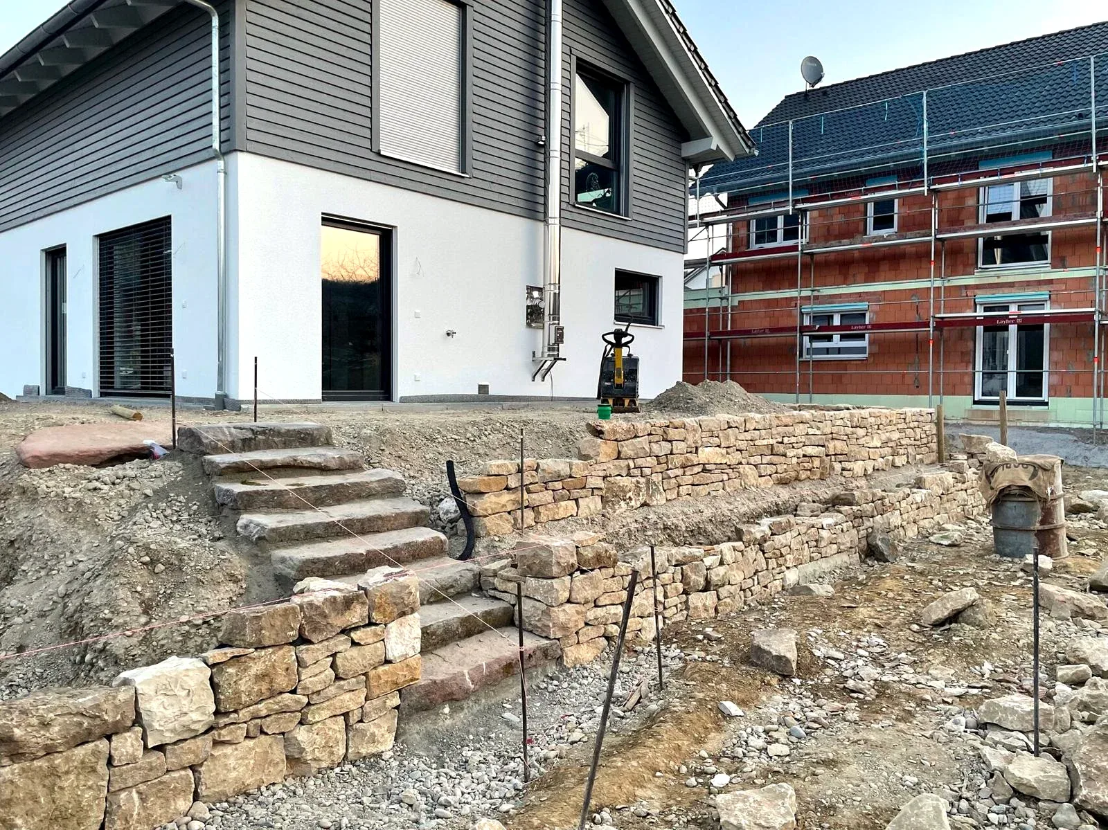Natursteintreppe zwischen gestaffelten Mauern vor dem Wohnhaus während der Bauarbeiten