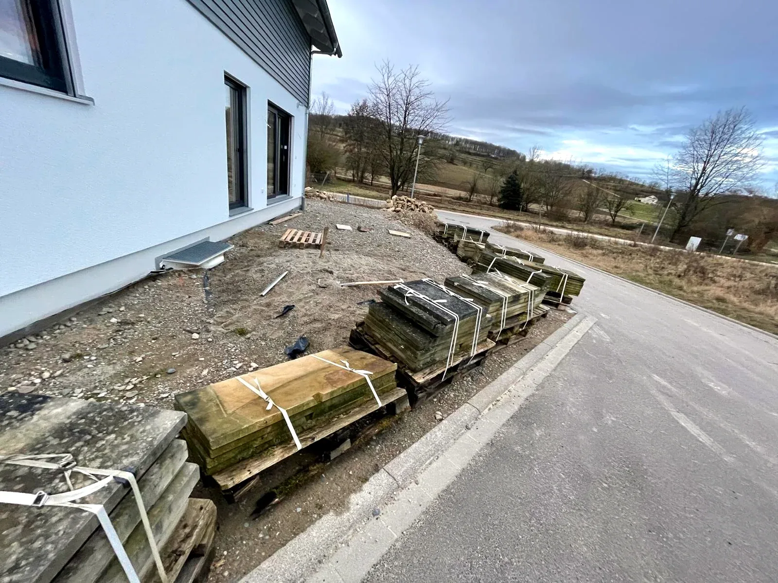 Unbebaute Außenfläche am grauen Wohnhaus mit bereitgelegten Natursteinen