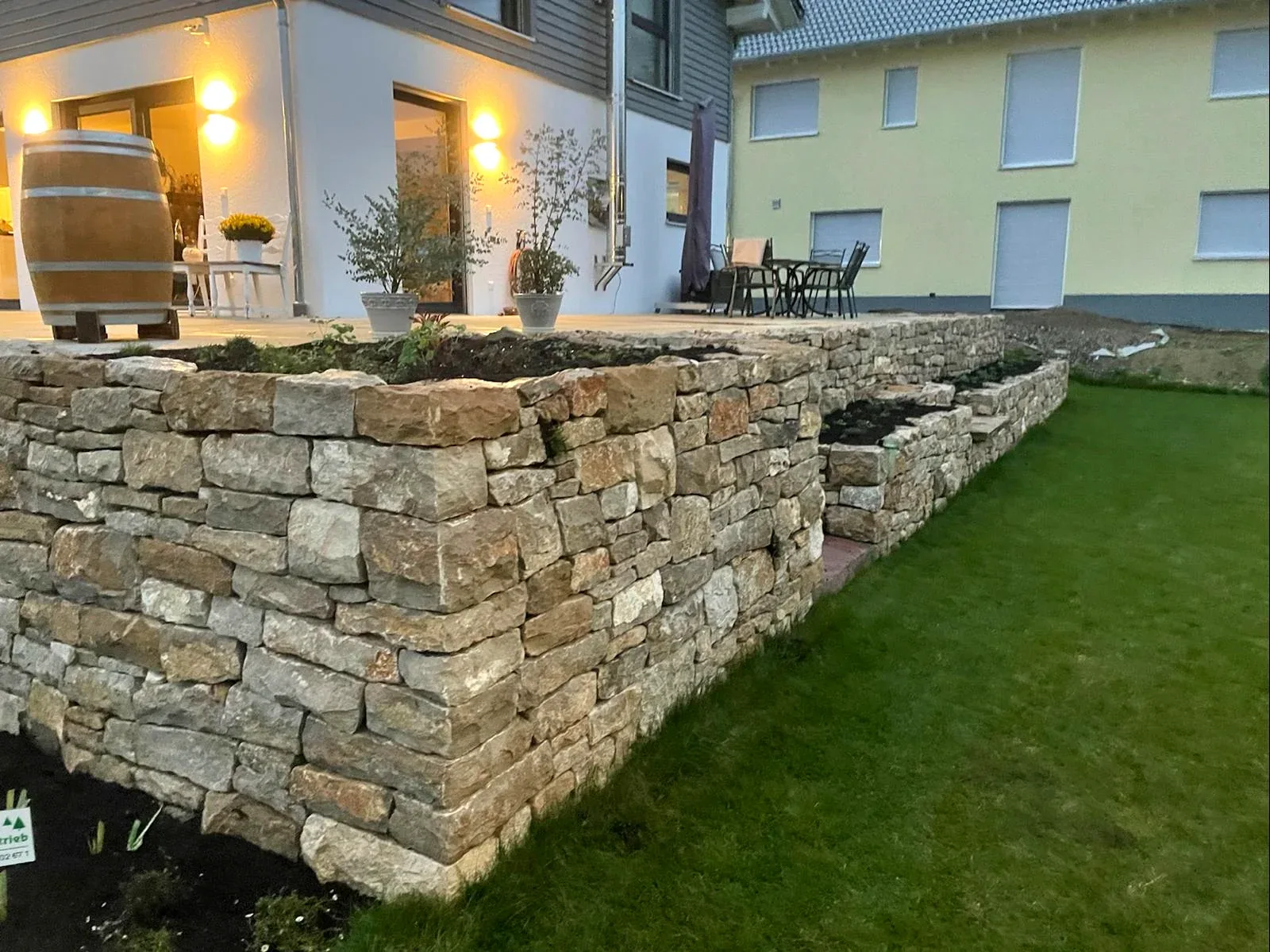 Gestaffelte Natursteinmauer mit Rasenfläche am Wohnhaus bei Abendlicht