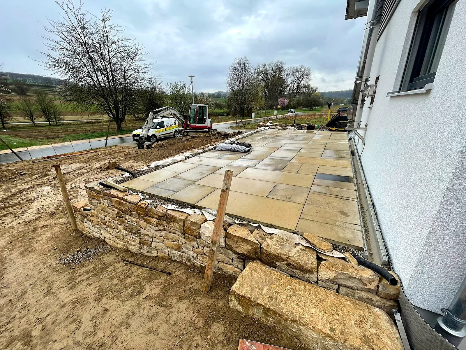 Terrassenplatten werden oberhalb der Natursteinmauer am Wohnhaus verlegt