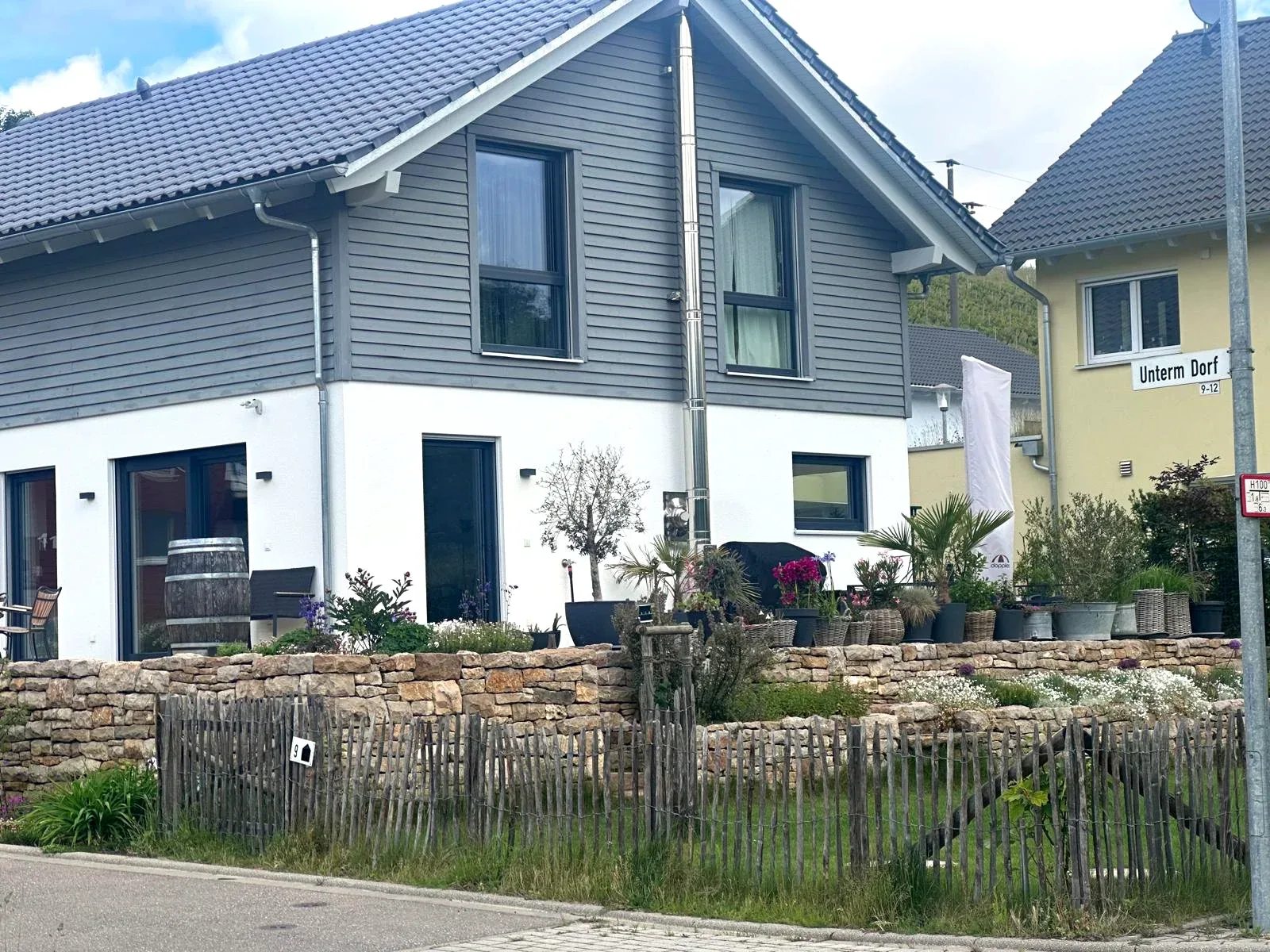 Bepflanzte Natursteinmauer vor dem grauen Wohnhaus
