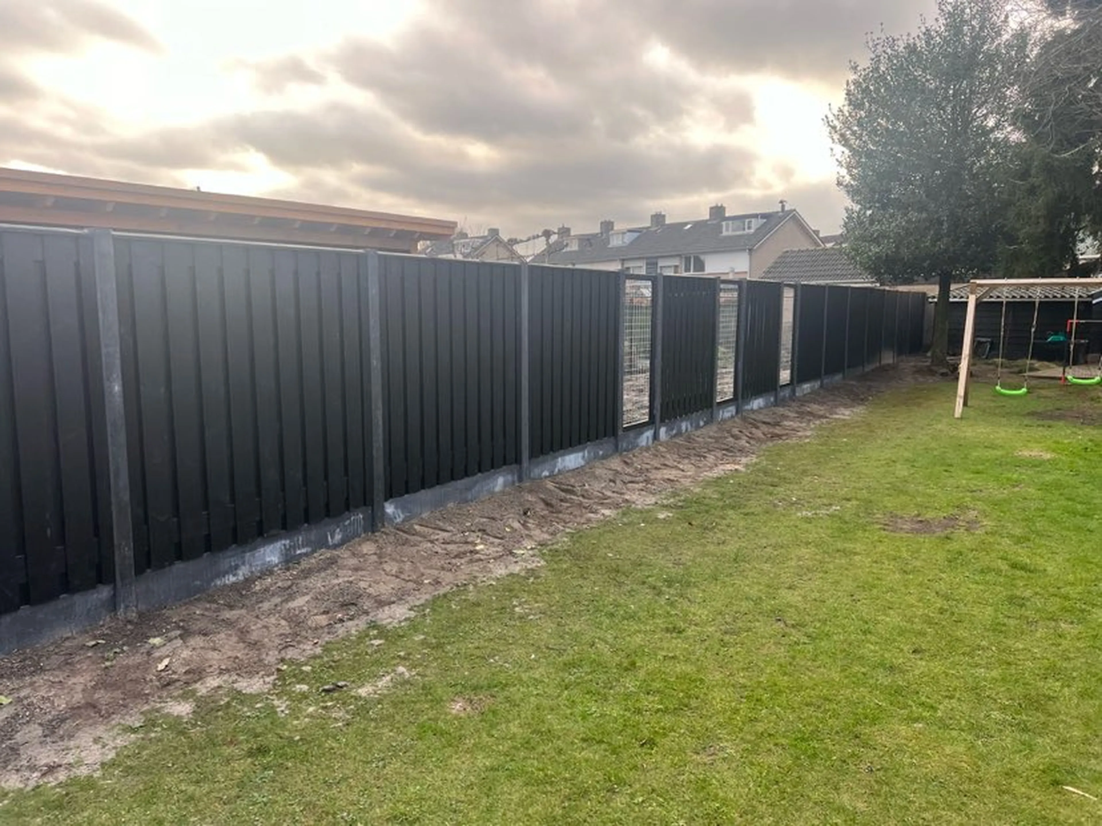 Stevige zwarte schutting met betonpalen in een tuin onder een donkere stormlucht