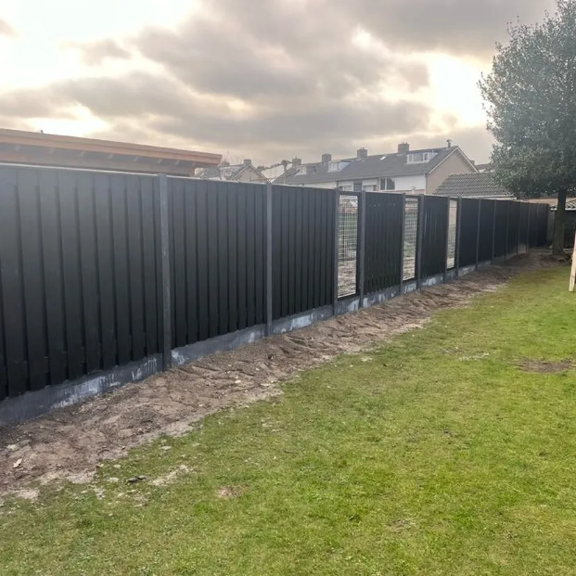 Stevige zwarte schutting met betonpalen in een tuin onder een donkere stormlucht