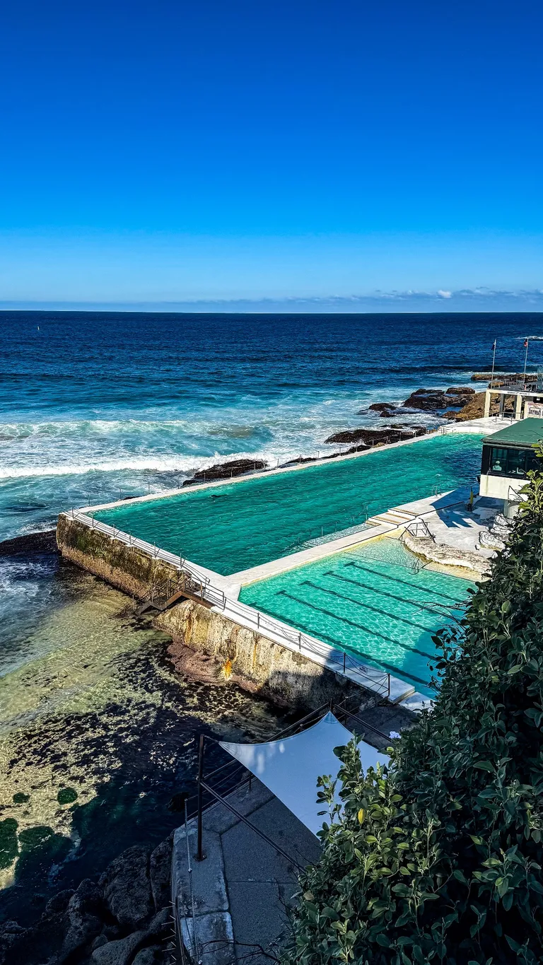 An ocean swimming pool on the coast, with blue water and surf beyond it.
