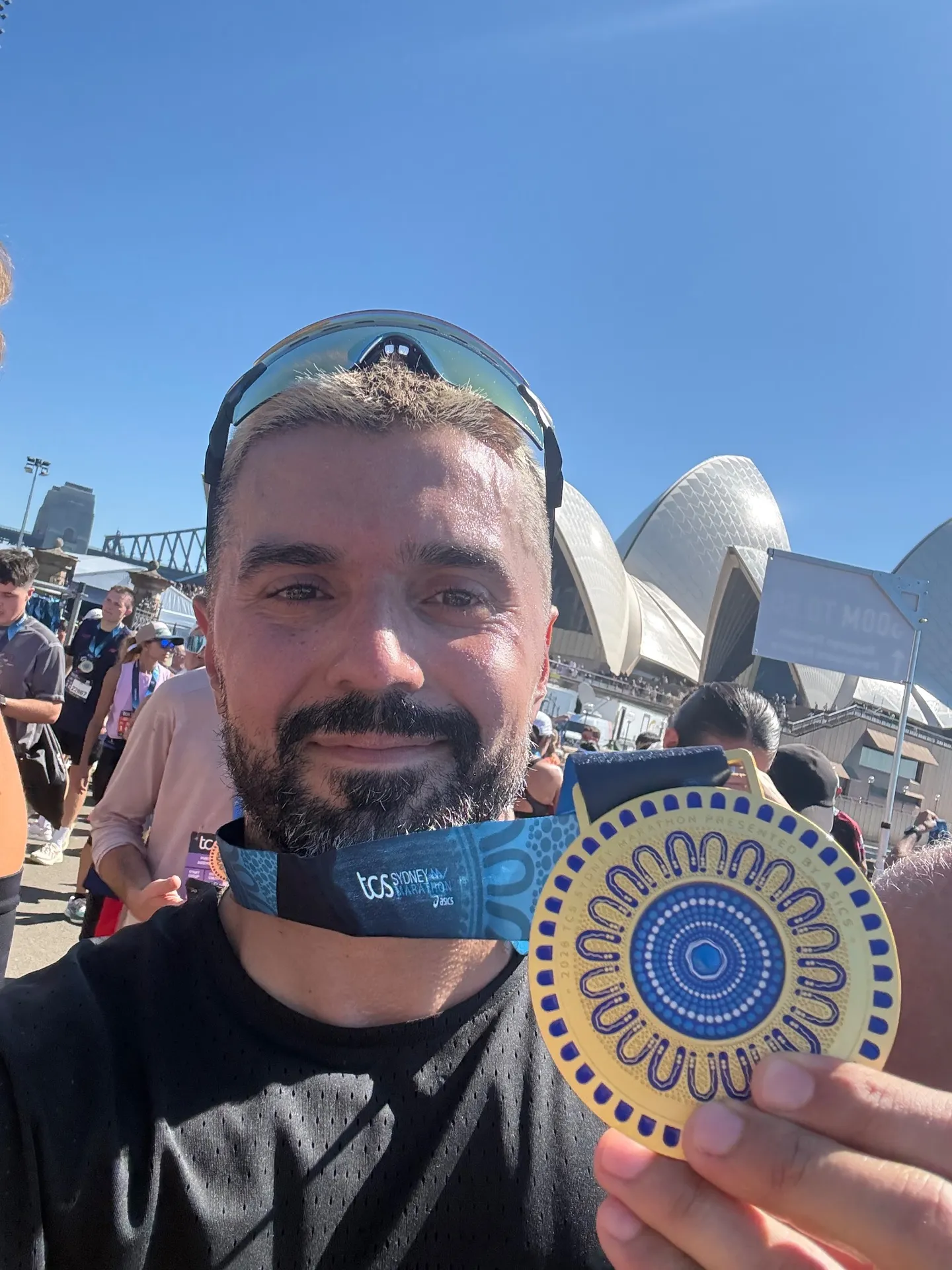 Serkan holds his finisher medal towards the camera, with the Sydney Opera House behind him.