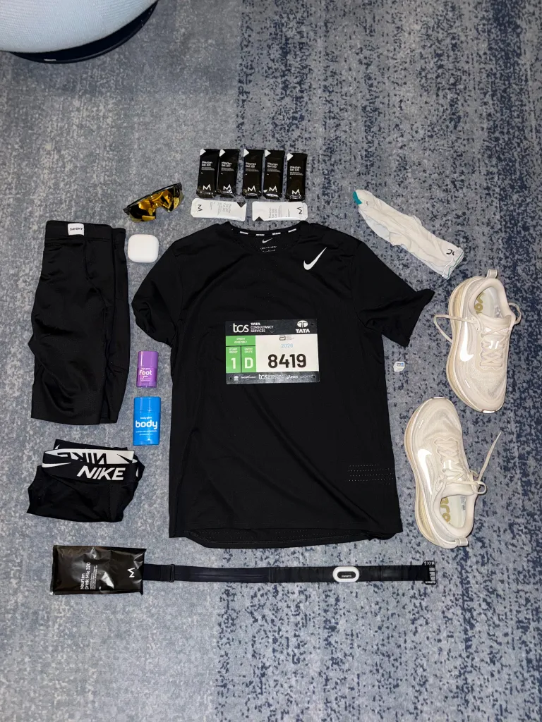 Running kit laid out with a black Nike outfit, race bib 8419, white running shoes and race nutrition.