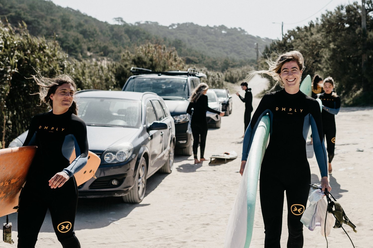 Two women in wetsuits smiling as they walk off the beach carrying surfboards