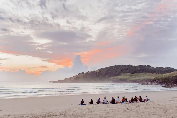 A group sitting on the beach at sunrise with a headland in the distance
