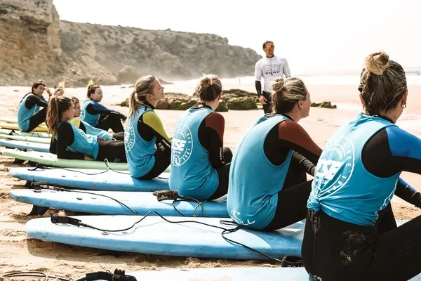 A group in wetsuits sitting on surfboards on the beach listening to a surf coach