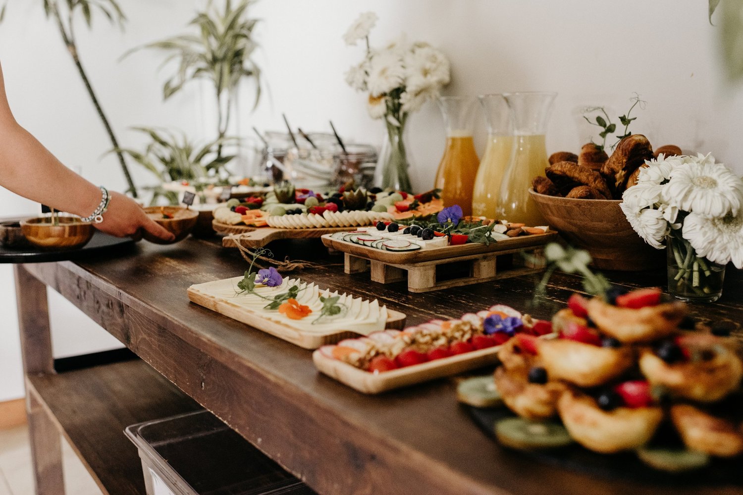 A breakfast table with fruit, pastries, juice and white flowers
