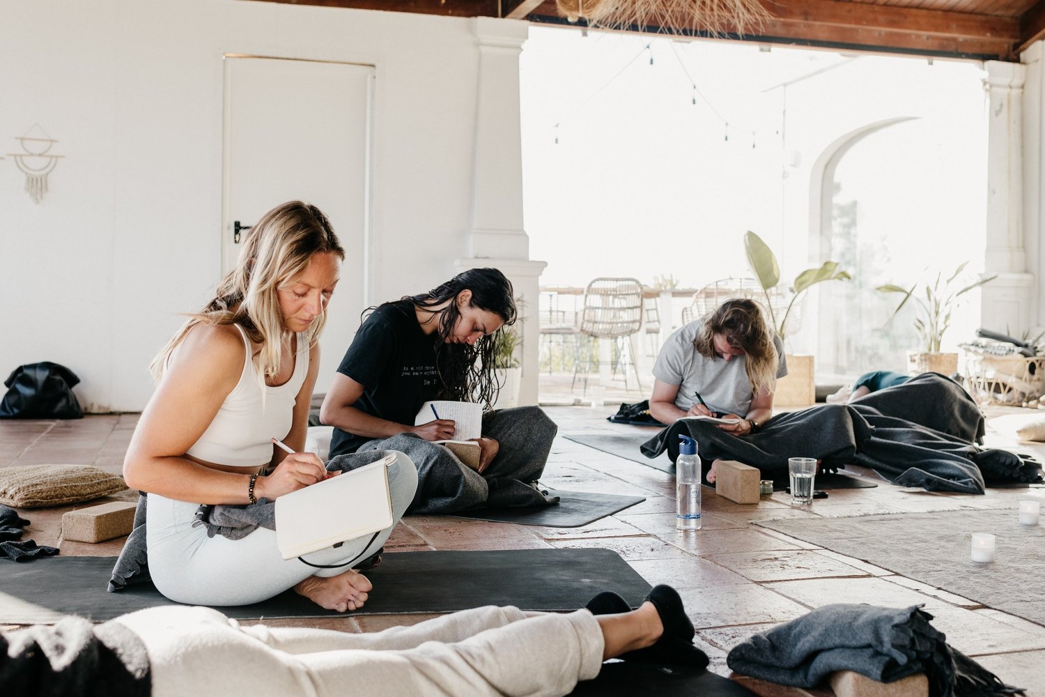 Three people journaling on yoga mats in a bright room