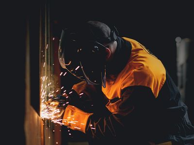 Industrial worker wearing protective helmet and gloves welding metal, with bright sparks flying, in a factory setting