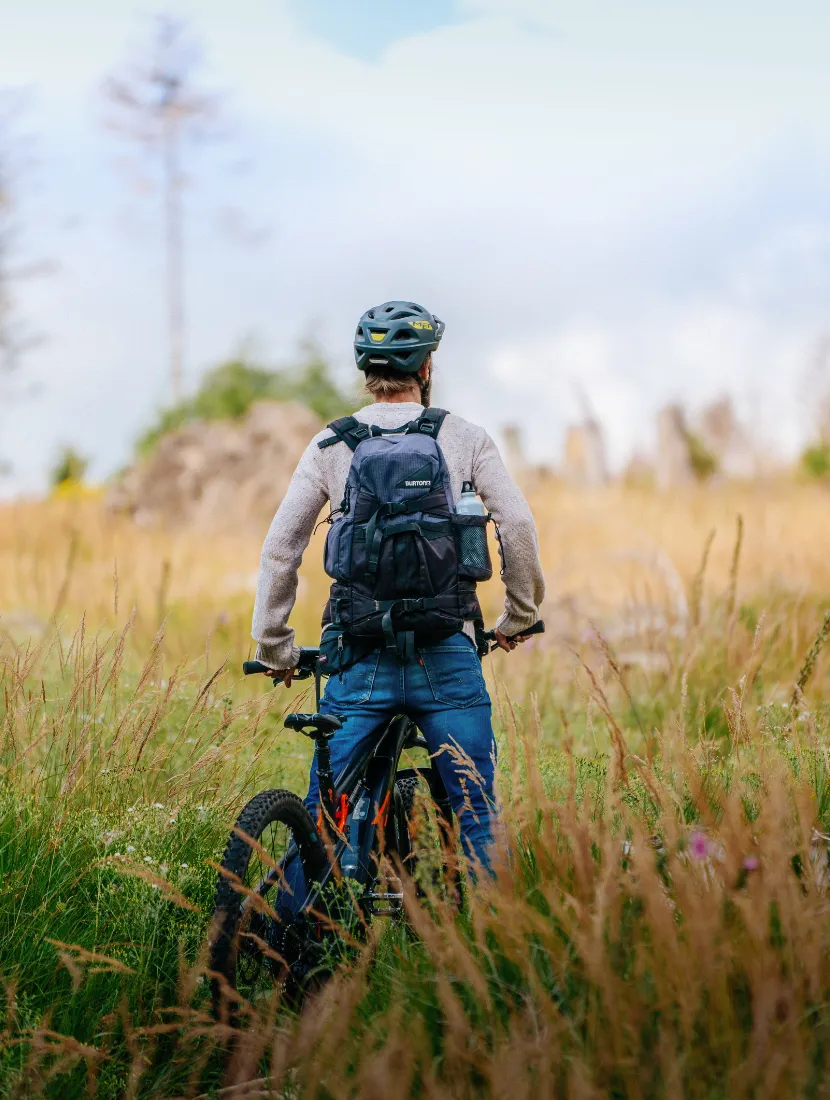 Bikeurlaub im Harz: Radfahrer mit Helm und Rucksack auf einem Trail durch hohes Gras