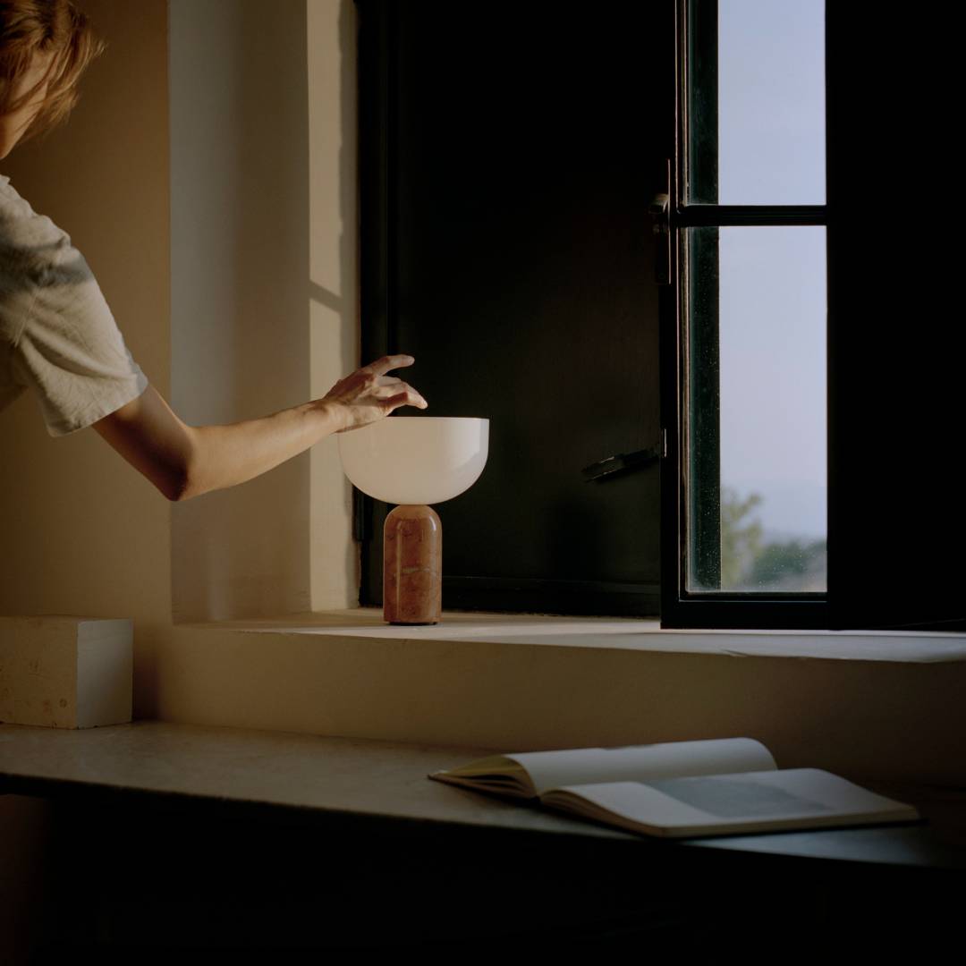 New Works Kizu asztali lámpa egy ablakpárkányon, lágy fénnyel, minimalista környezetben.