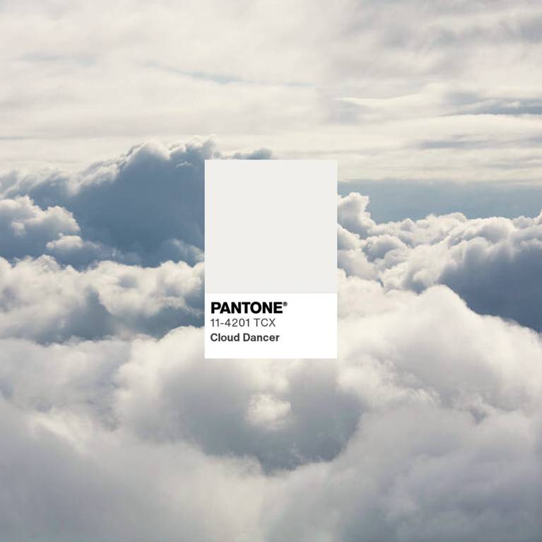 Pantone-Farbmuster "Cloud Dancer" vor weichen Wolken am Himmel - ein ruhiger, heller Weißton