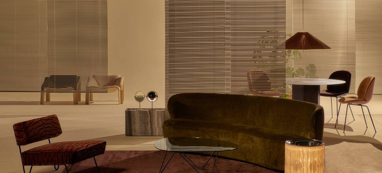 Et elegant rum med en blød, mørkegrøn sofa, glasbord og unikke lamper. Farvede stole og en trælampe ved et rundt spisebord skaber varme nuancer og sofistikeret belysning