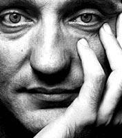 Close-up of a man with an intense gaze, his hand resting on his face. Black and white portrait with strong contrasts.